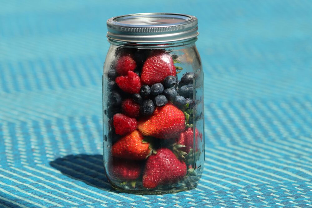 Glass jar filled with fresh strawberries and blueberries on a blue background, showcasing vibrant, antioxidant-rich fruits for immune support and cellular health.